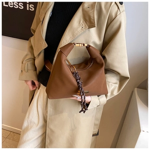 Détail d'un sac sous le bras marron foncé avec boucles dorées et breloque tressée chic