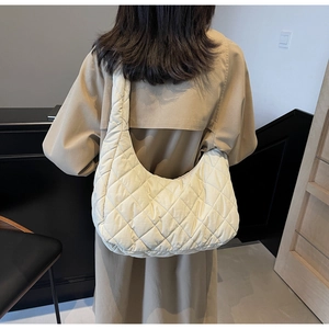 Quilted beige shoulder bag with soft padded texture and wide strap shown on a model