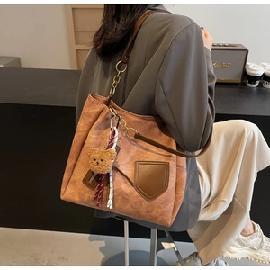 Detail of vintage brown leather tote bag with metal chain strap and cute bear charm