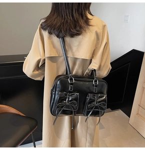 Detail view of glossy black tote bag with decorative bows and front flap pockets
