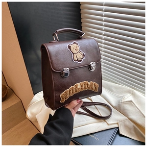 Close-up of brown leather backpack featuring a plush bear patch and silver snap closure