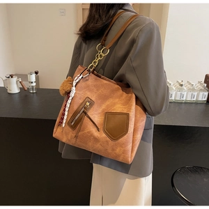 Detail view of large brown tote bag with metal chain strap and decorative charms