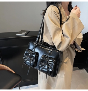 Detail of glossy black tote bag featuring double front pockets and bow decorations