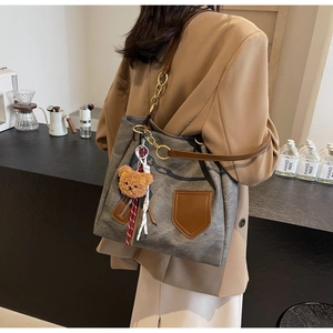 Detail of grey canvas tote bag with brown leather straps and plush bear charm