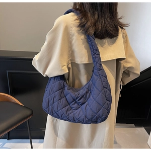Detail of dark blue quilted crescent bag worn with a beige trench coat for a stylish look