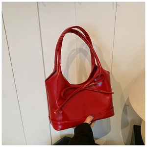 Détail d'un sac à main rouge en cuir avec un grand nœud décoratif et doubles poignées
