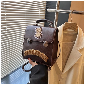 Close-up of brown vintage leather backpack with embroidered bear patch and buckle straps