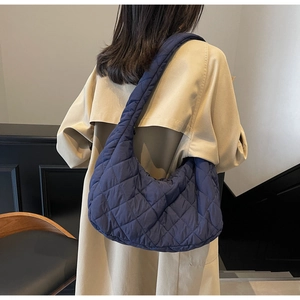 Detail of dark blue quilted puffer tote bag with rhombus pattern on model's shoulder