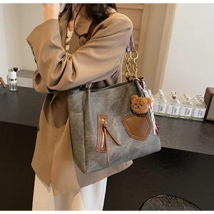 Detailed side view of canvas tote bag with brown leather trim and metal chain strap