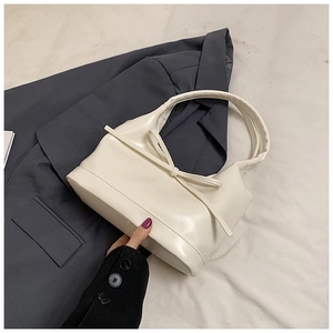 Détail du sac à main en cuir PU blanc crème avec nœud sur fond de blazer gris foncé