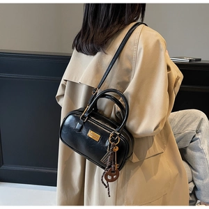 Detail einer schwarzen glänzenden Boston-Tasche mit goldenem Logo und Schlüsselanhänger