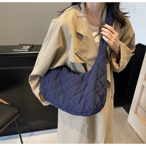 Side view of woman wearing a dark blue quilted crescent bag with wide shoulder strap
