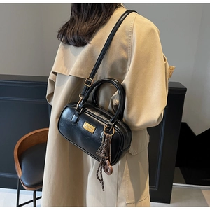 Detail einer schwarzen glänzenden Boston-Tasche mit Goldplakette und Schulterriemen