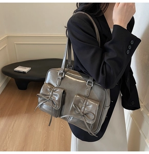 Detail of dark gray patent leather tote bag with dual front pockets and bow decoration