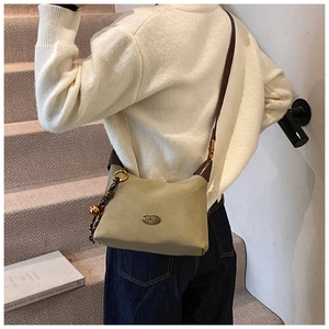 Détail du sac à bandoulière en daim vert sauge avec lanières en cuir brun et breloque