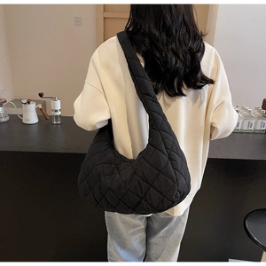Close-up of black quilted hobo bag with wide shoulder strap on a model in a cafe