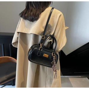 Detailansicht der schwarzen Boston Bag mit Goldplakette und geflochtenem Anhänger