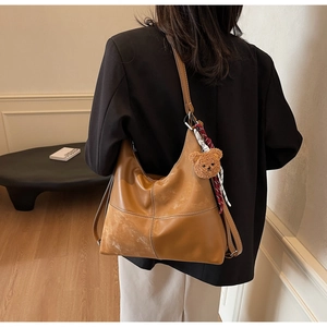 Détail du sac cabas en cuir marron avec surpiqûres blanches et pendentif ours décoratif
