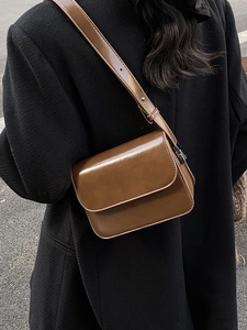 Brown leather crossbody square bag with flap and adjustable strap shown on model outdoors