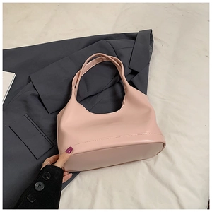 Détail d'un sac à main minimaliste rose pâle posé sur une veste de tailleur grise