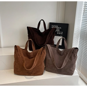 Three minimalist suede tote bags in earthy tones displayed on elegant marble stairs