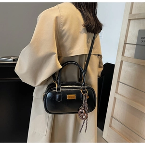 Detail einer schwarzen Boston Tasche mit Goldplakette und Anhänger an einem Model