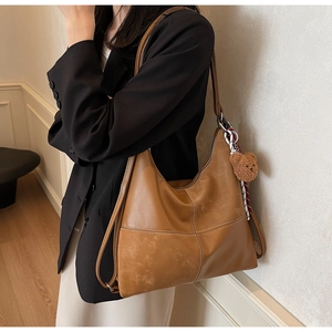 Détail d'un sac hobo marron avec coutures contrastées et un charmant ours en peluche