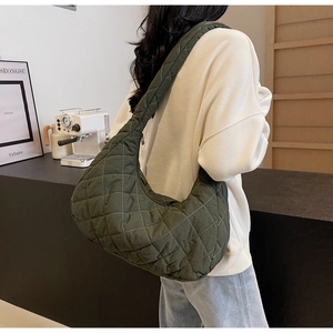 Close-up of quilted nylon crescent bag in dark green worn by a model in a minimalist room
