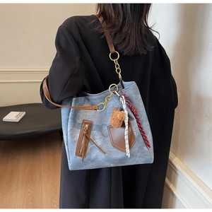 Detail of grey-blue denim tote bag with brown leather accents and plush bear charm
