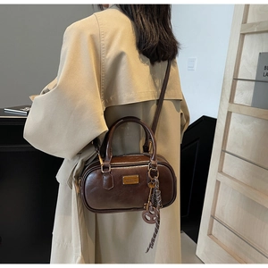 Makro-Detail der braunen Retro-Boston-Tasche mit Goldplakette und Schlüsselanhänger
