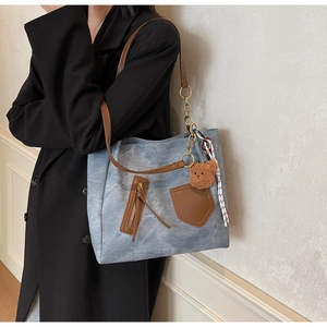 Detail of light blue canvas tote bag with brown leather straps and plush bear charm
