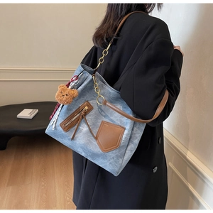 Detail of light blue marble-textured tote bag featuring brown leather trim and bear charm