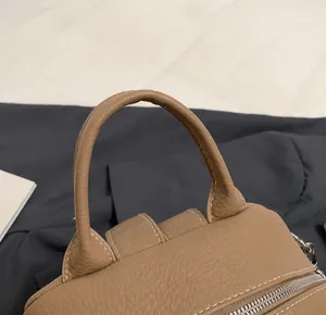 Detail der braunen Ledertasche mit Kieselstruktur, rundem Griff und weißer Kontrastnaht