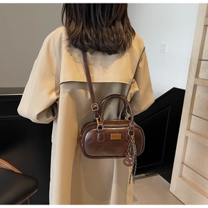 Detailsicht der hochglänzenden braunen Mini-Boston-Tasche mit goldener Plakette