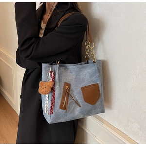 Detail of light blue washed tote bag with brown leather handles and plush bear charm