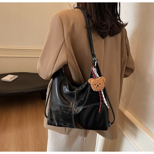 Détail d'un sac à bandoulière noir brillant avec surpiqûres blanches et charm d'ours mignon