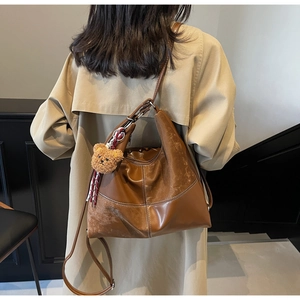 Détail du grand sac cabas en cuir marron avec breloque ours sur trench-coat beige