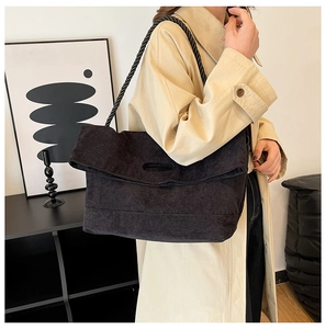 Detail of black corduroy tote bag with woven rope strap on model in beige coat