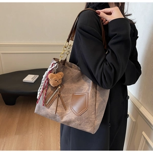 Detail of tan marble-textured tote bag with leather tassels and plush bear pendant