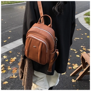 Nahaufnahme eines braunen Lederrucksacks mit drei Reißverschlussfächern und Metalllogo