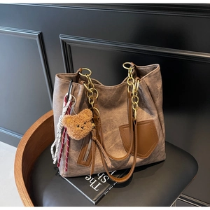 Detail of retro brown tote bag with chain strap, bear charm and woven rope on a chair
