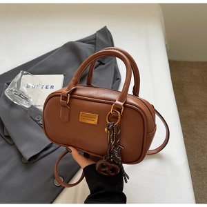 Detailansicht der braunen Vintage-Tasche mit goldener Plakette und Keks-Anhänger