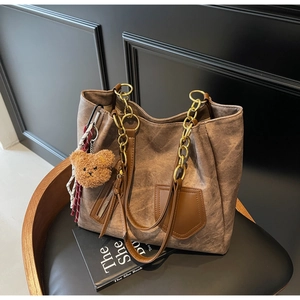 Detail of coffee brown tote bag with metal chain strap and cute teddy bear charm on a chair