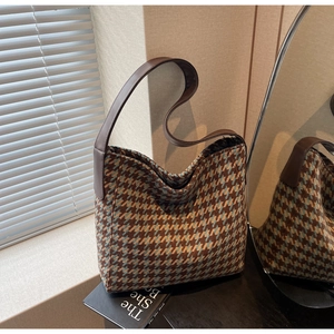 Close-up van houndstooth draagtas met bruine leren riem in een minimalistische kamer