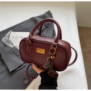 Detail der weinroten Bowling-Tasche aus Leder mit goldenem Logo-Schild und Tragegriff