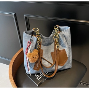 Detail of blue denim tote bag featuring brown leather strap and golden chain accent