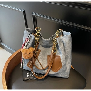 Detailed shot of denim tote bag with leather pockets, gold chain, and plush bear charm