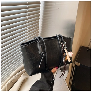 Detail of black faux leather tote bag with unique knot straps and baseball bag charm