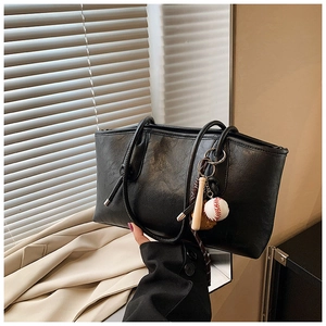 Detail of a black leather tote bag with baseball-themed charms and wrinkled texture