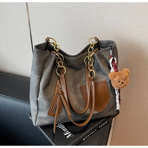 Detail of grey tote bag with gold chain strap, brown leather pocket and bear charm